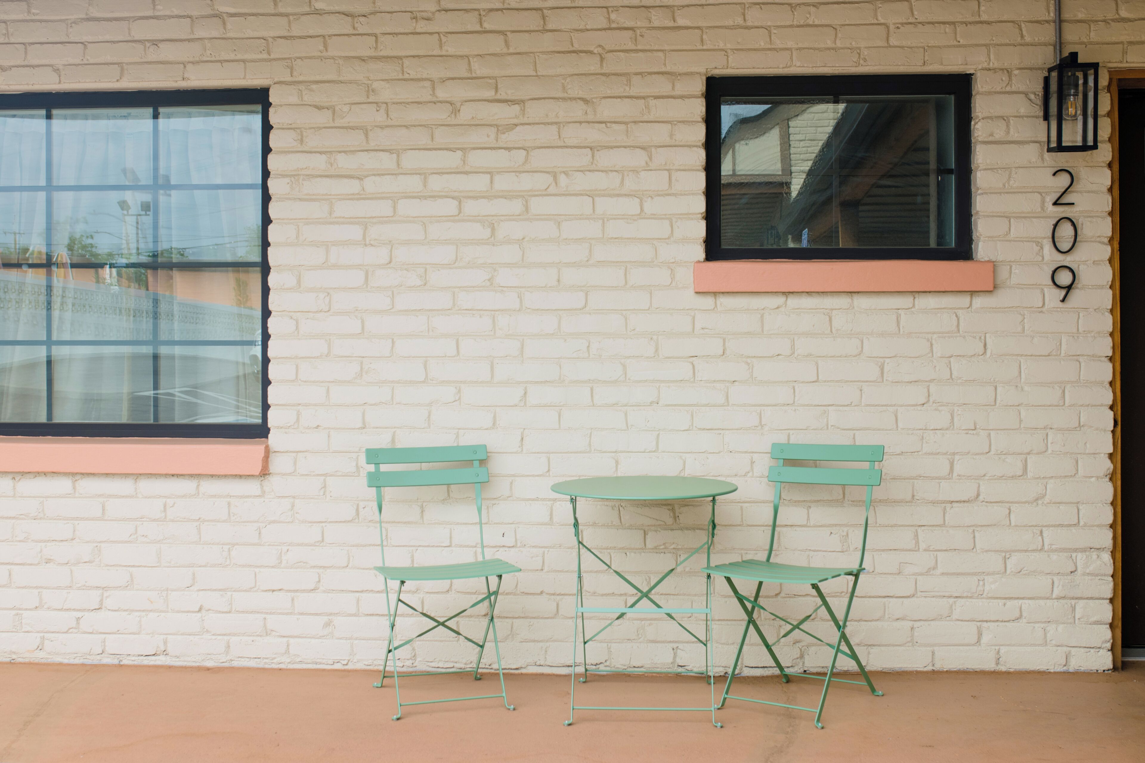 Pared de ladrillo blanco con dos sillas de metal verde y una mesa redonda pequeña.