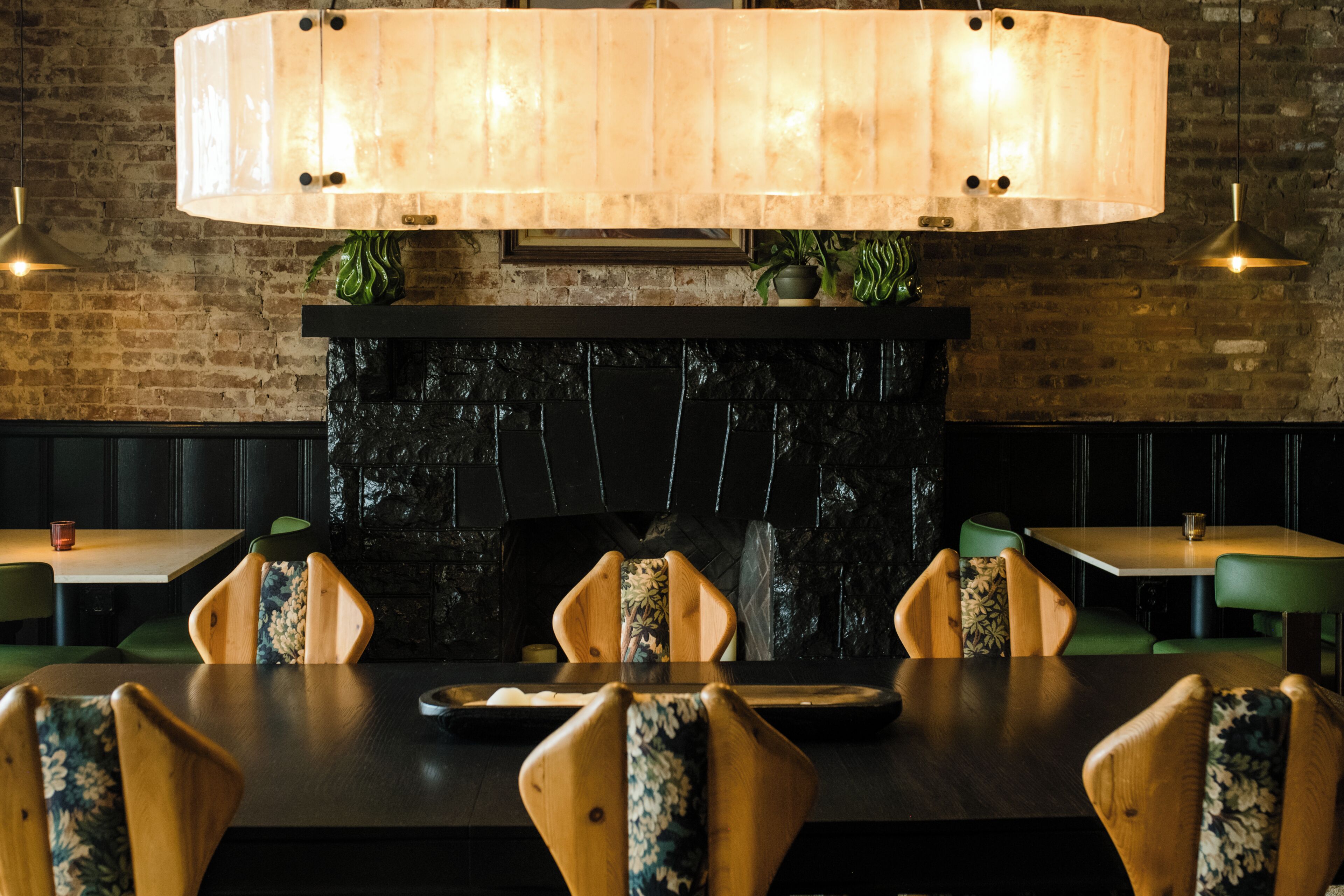 Ein Restaurant mit Backsteinwand, großem Holztisch und grünen Stühlen.