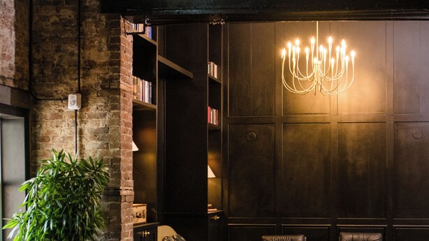 A modern interior with a wooden dining table, leather chairs, a chandelier, and a bookshelf. - Salt Ranch Hotel (Nashville)