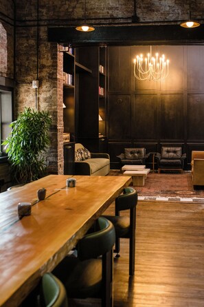 A modern interior with a wooden dining table, leather chairs, a chandelier, and a bookshelf. - Salt Ranch Hotel (Nashville)