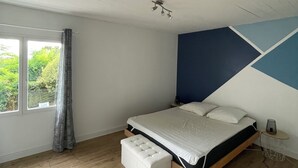 Ein Schlafzimmer mit Bett, einem Fenster mit Vorhängen, einem Nachttisch und einer Wand mit geometrischem Muster.