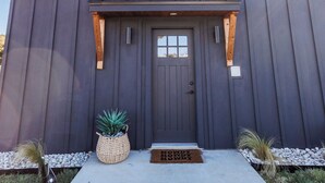 A modern building with a dark exterior, a front door, and a small porch area. - Charming 1-bedroom cottage in serene countryside (Blum)