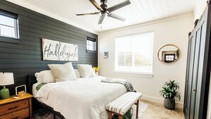 A bedroom with a bed, bedside table, nightstand, bench, ceiling fan, window, and a mirror. - Charming 1-bedroom cottage in serene countryside (Blum)