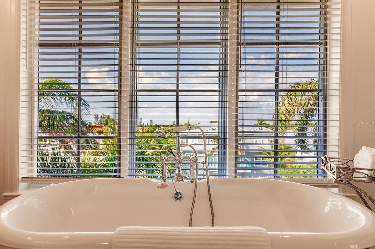 Ein Badezimmer mit einer großen Badewanne, einer Dusche und einem Fenster mit Jalousien.