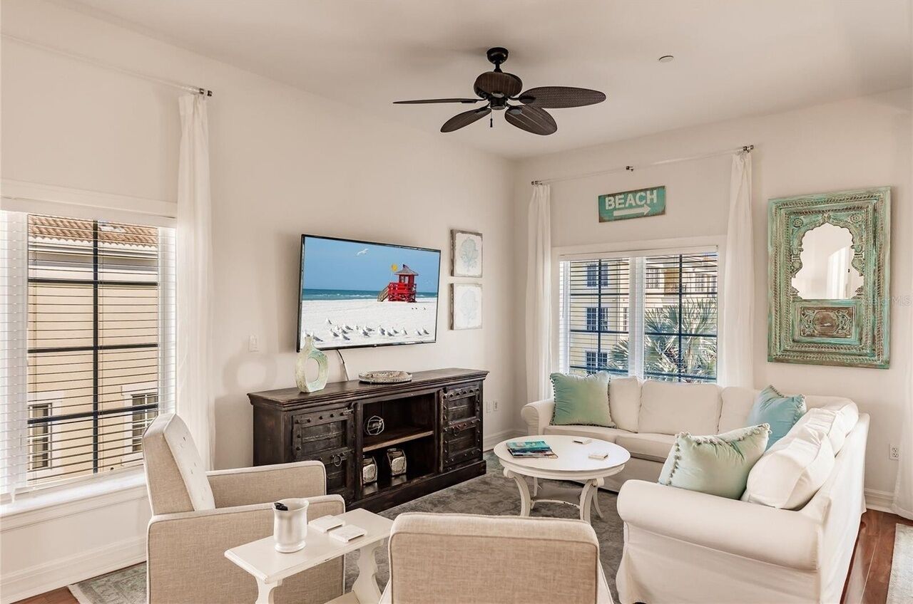 A living room with a television, a ceiling fan, a couch, a coffee table, and a sign that reads "BEACH".