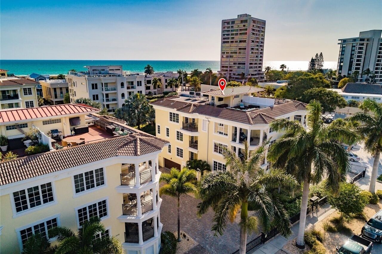 A multi-story hotel with balconies, a view of the beach, and palm trees.