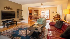 A living room with a TV, a coffee table, a red sofa, and a dining area in the background. - Base yourselves here!  3 bes+2ba w/ great yard, dual monitor workstation! (Lawrence)