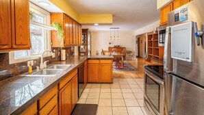 A kitchen with wooden cabinets, a stainless steel refrigerator, a sink, and a dining area with a table and chairs. - Base yourselves here!  3 bes+2ba w/ great yard, dual monitor workstation! (Lawrence)