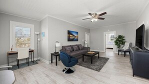 Een moderne woonkamer met een grijze bank, een blauwe fauteuil, een salontafel en een televisie.