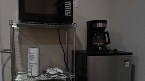 Una cocina equipada con microondas, cafetera y refrigerador. Hay contenedores de almacenamiento en un estante metálico.