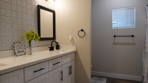 Un baño con tocador blanco, espejo, lavabo y toallero.