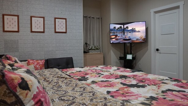 Un dormitorio con cama, televisor montado en la pared y cuadros enmarcados.