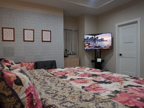 Un dormitorio con cama, televisor montado en la pared y cuadros enmarcados.