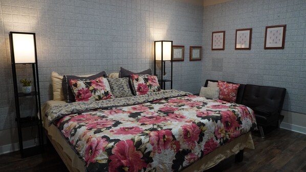 Un dormitorio con una cama grande, dos mesitas de noche, un cabecero y una pared de ladrillo gris con cuadros enmarcados.