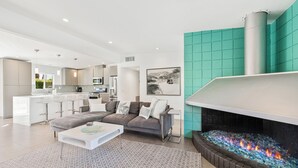 Een moderne woonkamer met een open haard, een keuken op de achtergrond en een wand in turquoise.