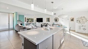 Een moderne keuken met een centraal eiland, hanglampen en uitzicht op de woonkamer.