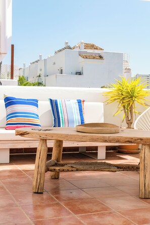 A terrace with a wooden table, a white sofa with striped cushions, and a potted plant. - Luxury Penthouse • Rooftop •  Sea views • Private Parking (Estepona)