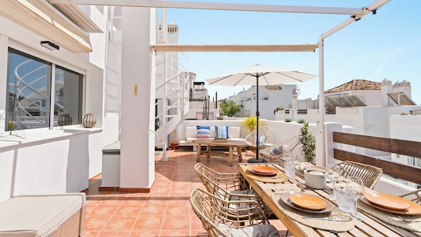 An outdoor terrace with a wooden table set for dining, wicker chairs, and a white railing. - Luxury Penthouse • Rooftop • Sea views • Private Parking (Estepona)