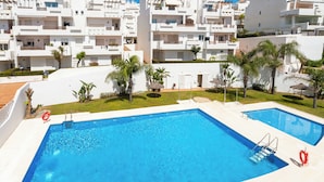A swimming pool with two ladders, surrounded by a white building with balconies and palm trees. - Luxury Penthouse • Rooftop • Sea views • Private Parking (Estepona)