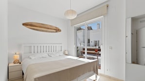 A bedroom with a bed, bedside lamps, a wooden shelf, and a view through a glass door. - Luxury Penthouse • Rooftop • Sea views • Private Parking (Estepona)