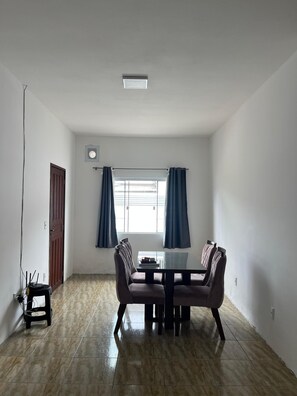 Una habitación amplia con una mesa de comedor y sillas, una ventana con cortinas, una puerta y una lámpara en el techo.