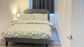 Un dormitorio con cama, mesita de noche, lámpara, una lámpara colgante con forma de estrella y una ventana con cortinas.