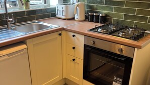 Una cocina compacta con gabinetes blancos, horno integrado, fregadero y estufa.