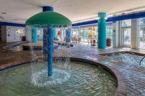 An indoor pool area with multiple water features, including a central fountain and smaller water jets. - Beachfront Boardwalk Condo (Myrtle Beach)