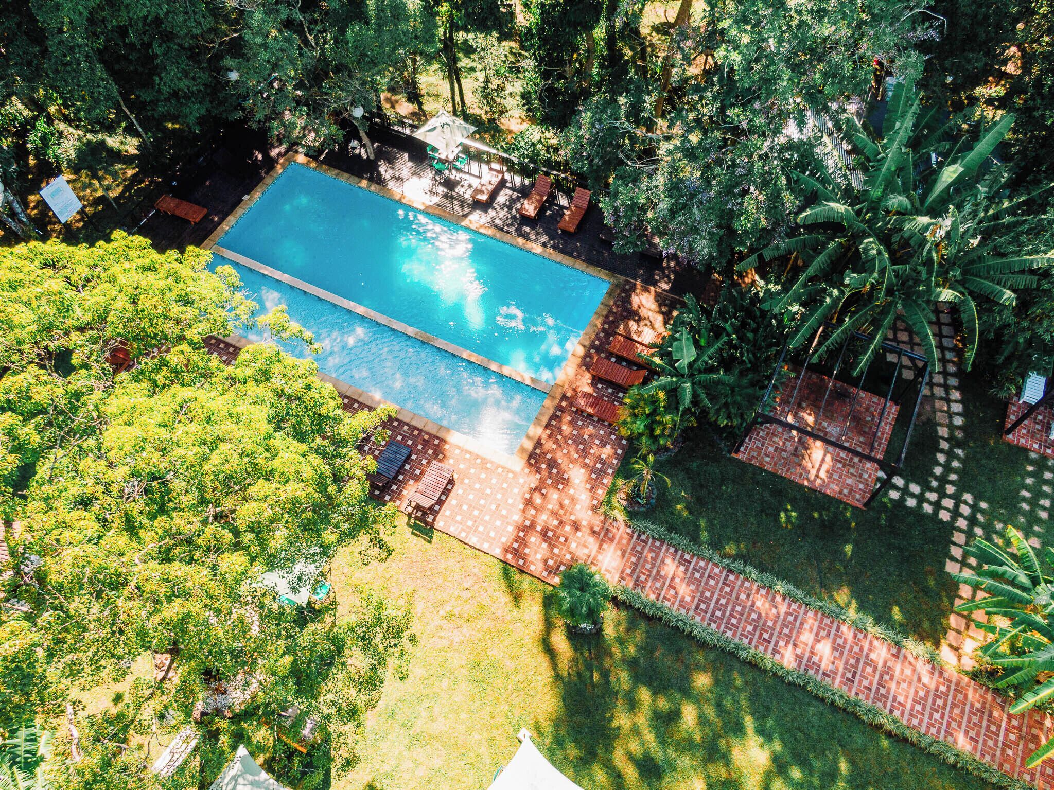 Vista aérea de uma área de piscina com uma piscina retangular, rodeada por vegetação exuberante e um caminho de tijolos.