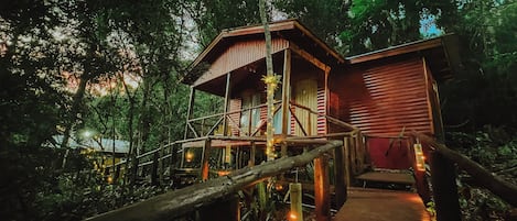 A wooden cabin with a balcony, surrounded by dense forest.