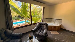 A modern room with a large window, a jacuzzi, two leather armchairs, and a small table with a bottle and glasses.