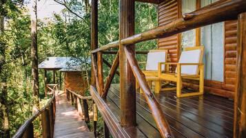 Una terraza de madera con barandillas que lleva a una cabaña con dos sillas y una mesa.