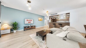 A modern living room with a sofa, coffee table, and a 'BOOK ME' sign on the wall. - Stayshort - 2 Bed in Dubai Marina That Sleeps 5 (Dubai)