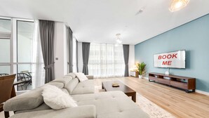 A modern living room with a sectional sofa, a TV mounted on the wall, and a dining area visible through a glass door. - Stayshort - 2 Bed in Dubai Marina That Sleeps 5 (Dubai)