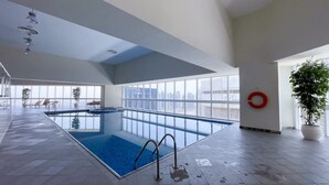 An indoor swimming pool with clear glass walls, a lifebuoy, and a potted plant. - Stayshort - 2 Bed in Dubai Marina That Sleeps 5 (Dubai)