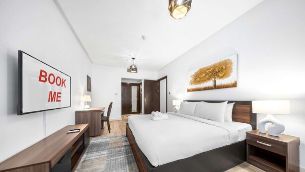A modern hotel room with a large bed, a desk, a chair, a TV, and a painting on the wall. - Stayshort - 2 Bed in Dubai Marina That Sleeps 5 (Dubai)
