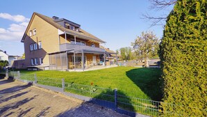 A two-story house with a covered patio, a fenced yard, and a well-maintained lawn. - Henno's Apartment (Bielefeld)