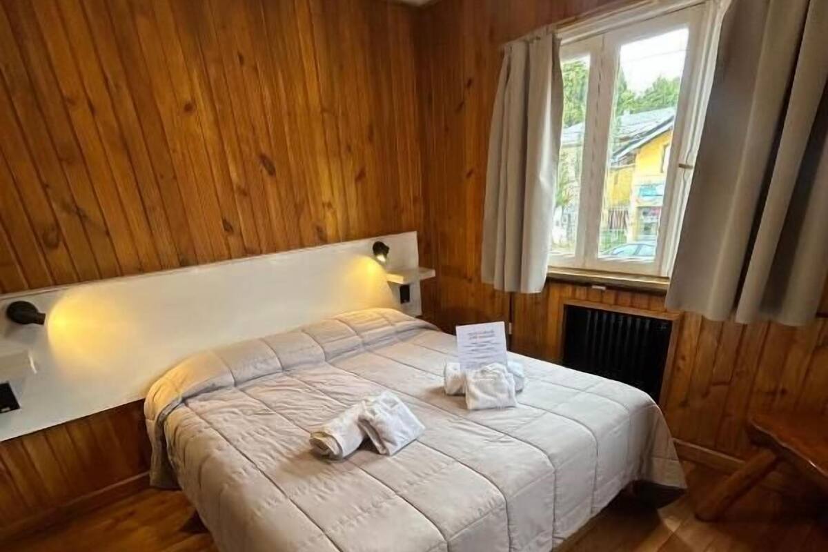 Une pièce aux murs lambrés, comprenant un lit, une table de chevet et une fenêtre avec des rideaux.