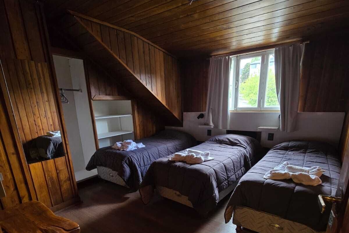 A cabin-style room with two beds, a wooden ceiling, and a window with curtains.