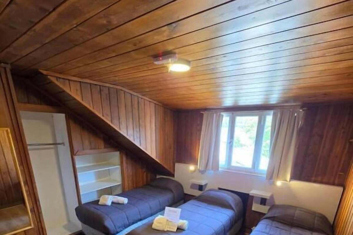Une cabane aux murs et au plancher en bois, avec deux lits, une petite cuisine et une fenêtre.