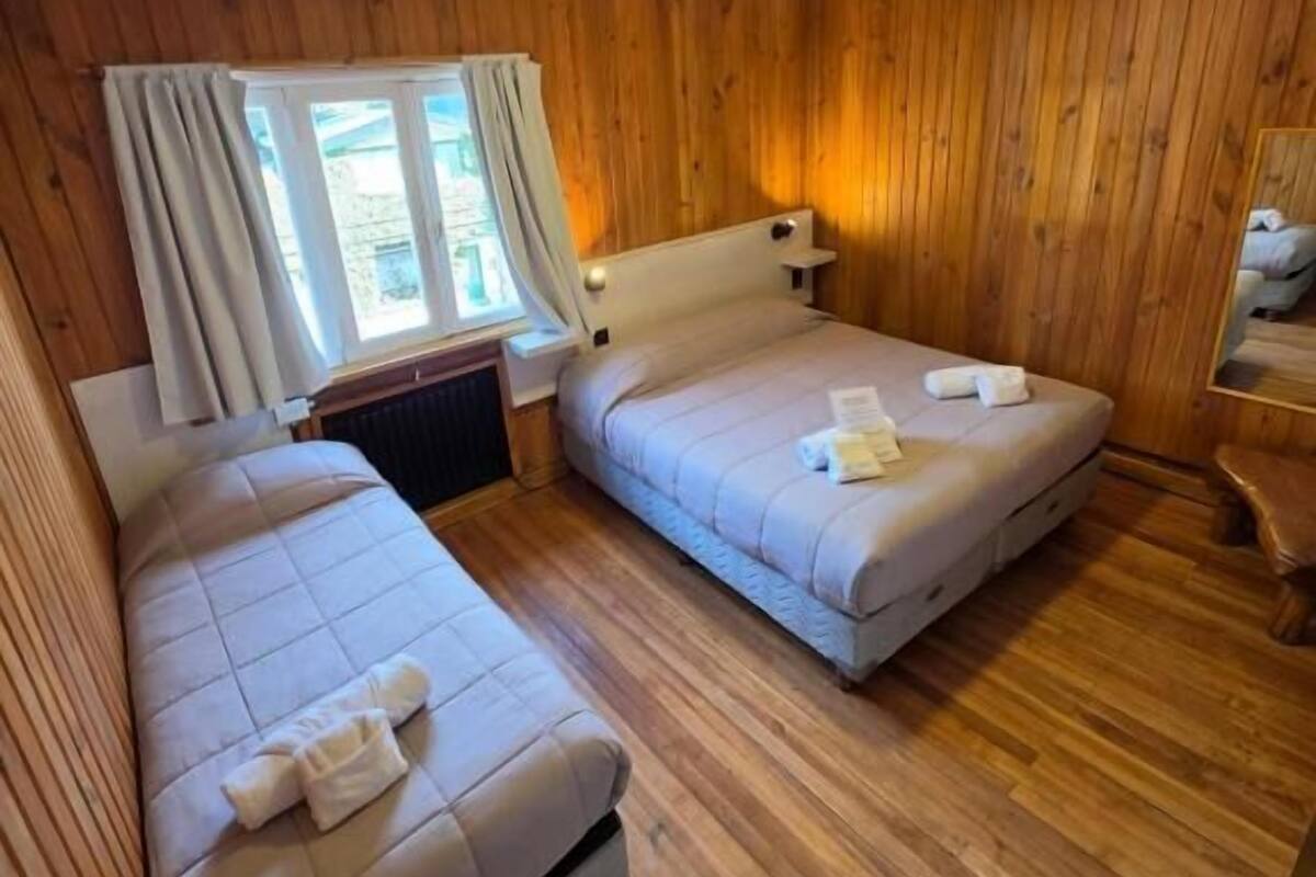 Une pièce avec des lambris en bois, deux lits avec des oreillers et des serviettes, une fenêtre avec des rideaux et une petite table.