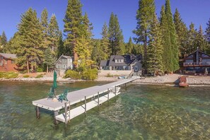 A waterfront property with a dock, clear water, and houses surrounded by tall trees. - Lake House with Pier and Buoy (Tahoe Vista)