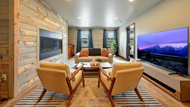 Una sala de estar moderna con un sofá, dos sillones, una mesa de centro, un televisor de pantalla plana y una pared de madera.