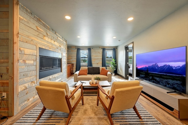 Una sala de estar moderna con un sofá, dos sillones, una mesa de centro, un televisor de pantalla plana y una pared de madera.