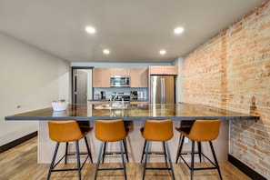 A modern kitchen with a central island, bar stools, and a brick wall.