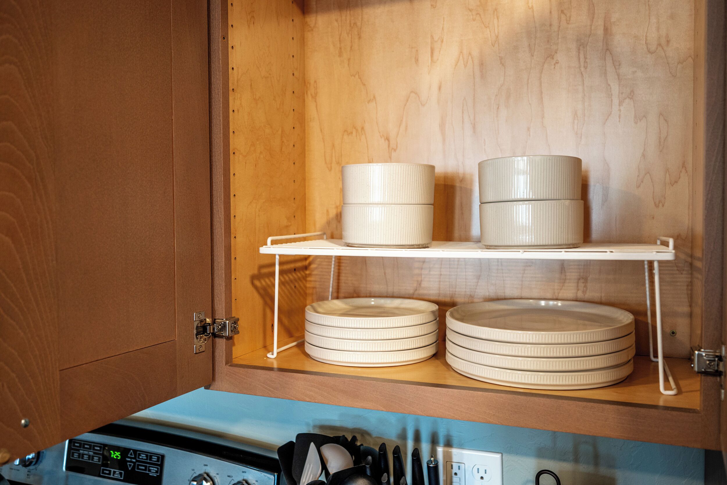 A kitchen cabinet with a wooden interior, a white shelf holding stacked bowls, and a dishwasher below.
