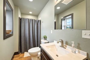 A bathroom with a toilet, shower curtain, sink, and mirror.