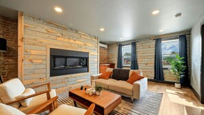 Una sala de estar moderna con chimenea, paneles de madera, un sofá, una mesa de centro y un amplio ventanal con cortinas.