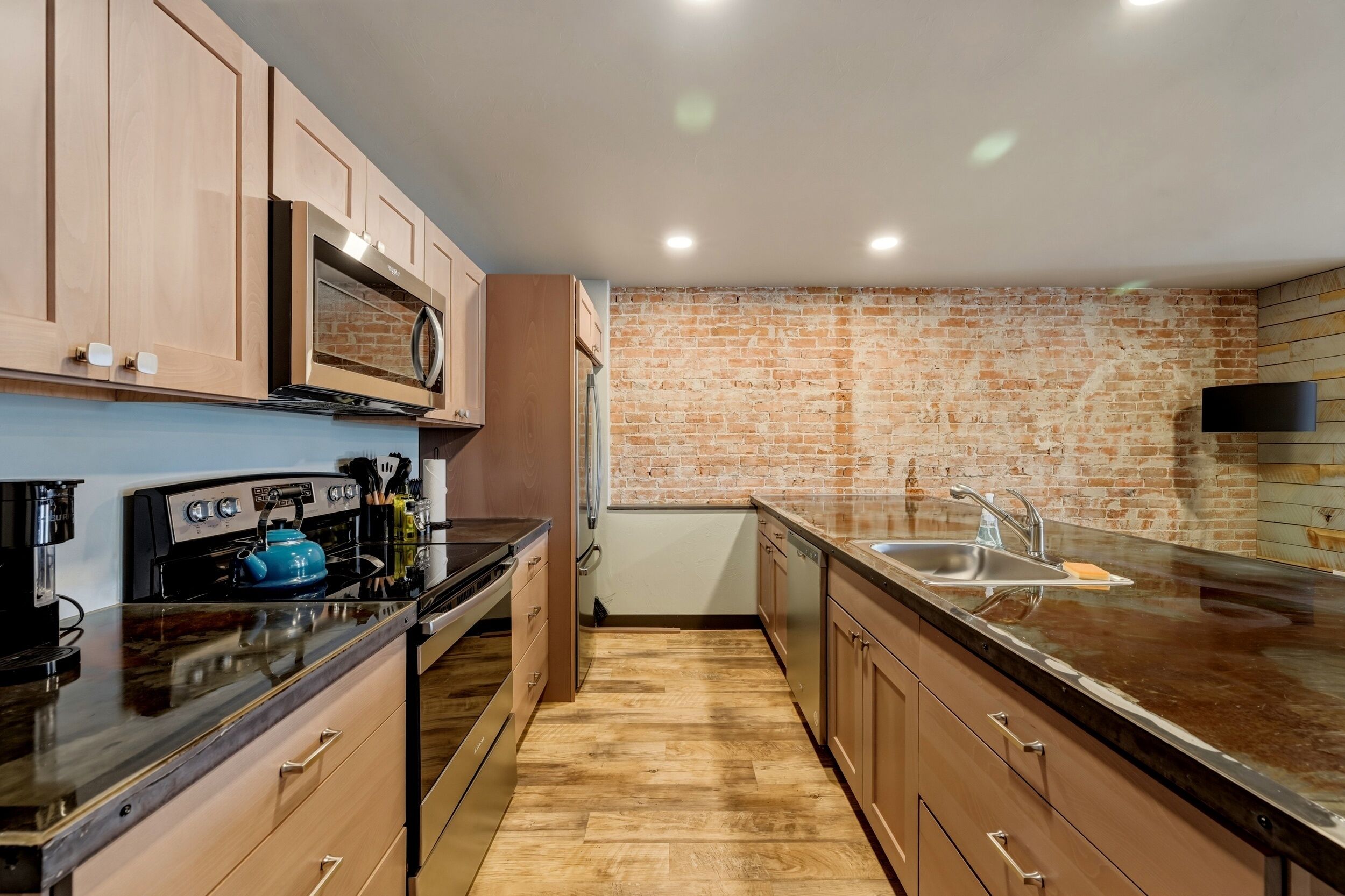 A modern kitchen with wooden cabinets, a brick wall, and a stainless steel sink.