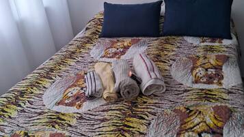 A bed with a tiger-patterned quilt, two pillows, and rolled towels.